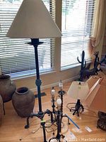 Four lamps displayed near windows with blinds, including two tall floor lamps and two table lamps with cords and light beige fabric shades.