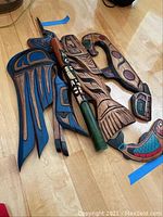 Five Native American tribal art pieces laid on wooden floor, showing bird, fish, flute, and serpent figures with painted and carved details.