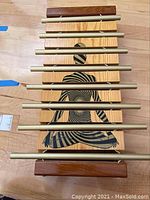 Front view of the chakra xylophone showing seven metal bars and meditating figure design on wooden base, with two wooden mallets on top.