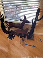 Five metal sculpture artworks on a wooden floor near a window, depicting a Kokopelli, a moose, and a baby deer among others.