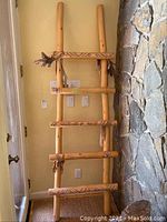 Photo of Southwestern wooden ladder with smooth wood poles and some rope accents leaning against stone wall.