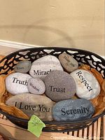 Photo of a black metal basket filled with smooth meditation stones, each engraved with positive or inspirational words.