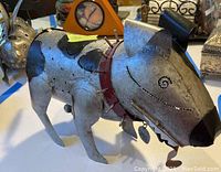 Side and front views of the metal dog sculpture showing detailed features including black spots, collar with spikes, and metal tags.