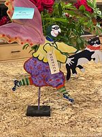 Whimsical fairy holding a black and white cat, painted in yellows, purples, greens