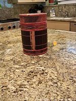 Single cylindrical Indonesian basket with dark woven fibers and red bindings placed on granite countertop.