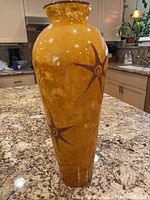 Tall orange glass vase with decorative brown stars on marbled orange background, standing on kitchen counter.