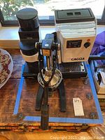 Photo showing coffee grinder, espresso machine, and manual citrus press on a wooden surface by a window.