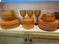 Amber glass plates, stacked small and large bowls, and three decorated wine goblets on shelf
