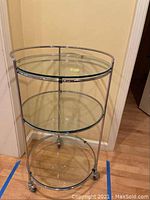 Front view of three-tier round bar cart with glass shelves and metal frame on caster wheels.