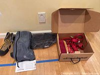 Climbing shoes, mesh bag, and cardboard box with climbing equipment on a wooden floor against a wall.