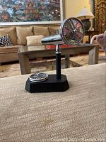 Tabletop kaleidoscope on black octagonal base with additional color wheel flat on base, shown on fabric surface