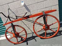 Full side view of red-painted wooden and iron bicycle against cinder block wall