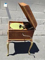 Front view of antique phonograph with lid open, showing green felt turntable and crank handle on side.