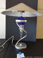 Photo of full lamp with conical shade, blue glass orb, spiral metal frame, and cord showing.