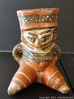 Front view of the polychrome tripod vessel showing anthropomorphic figure, tripod legs, and facial details