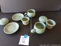 Full set of 3 cups and 3 matching saucers shown on a black surface. Cups have light green celadon glaze with delicate crackle and floral relief decoration.