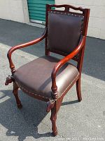 Front and side view of wooden chair with brown cushioned seat and backrest with stud detailing. Carved horse head sculptures on front legs and curved armrests visible.