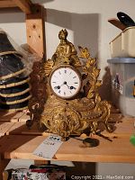 Front view of gilded metal mantel clock with seated female figure and white enamel dial