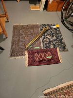 Overview photo of two wool rugs, synthetic floor mat, and three curtain rods arranged on floor.