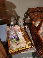 View of four white metal tea light lanterns with star-shaped cutouts next to a stack of framed prints, lavender soap set sealed in plastic wrapping with a small towel, and a blue storage bin.
