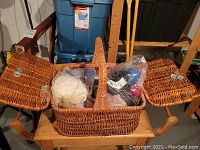 Wicker basket with two open lids showing bags of wool yarn and other knitting materials inside