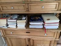 Stacked cookbooks on a wooden sideboard, some with visible titles, one book with a stain on cover.