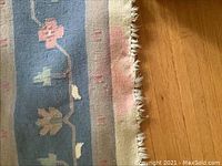 Close-up showing blue floral border and cream fringe with visible orange stain on rug fringe and edge.