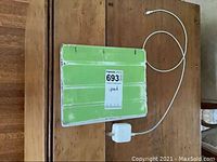 iPad closed in green protective case with charger cable and plug visible on wooden table