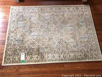 Top down photo showing full rug with detailed traditional floral and geometric patterns in muted neutral tones, placed on hardwood floor.