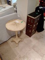 Photo of round wooden table with worn top surface next to a sofa and the multi-drawer cabinet.