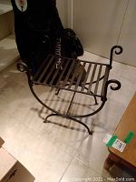 Metal bench viewed from an angle showing its curved legs and curled armrests, slatted seat made of metal strips.