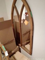 Full view of arched wooden frame mirror leaning against wall. The mirror is divided vertically into three sections by thin wooden strips. Shows overall design and size.