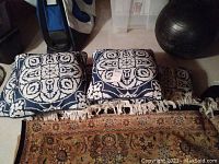Five navy and white patterned outdoor pillows with fringe displayed on floor with carpet and exercise ball visible.