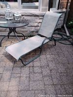 Full view of outdoor chaise lounger showing metal frame and fabric seating on stone patio.
