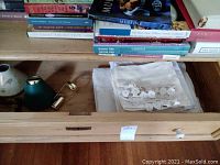 Drawer contains folded white and lace-trimmed napkins and tablecloths alongside several books on top shelf.