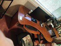 View of curved multi-level wooden desk with computer monitor, keyboard, lamp, and office chair.