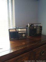 Two vintage Panasonic radios placed on a wooden surface next to a window with blinds, showing overall condition and design features.