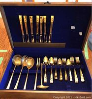 Full view of the opened blue velvet-lined wooden box containing brass serving utensils and Community Plate flatware including knives, forks and spoons.