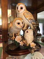 Front view of barn owl family figurine showing three owls on branch with flowers and wooden base.