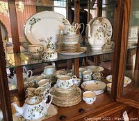 view of two shelves of Royal Albert White Dogwood bone china including serving platters, teapot, creamer, sugar bowl, stacks of plates, cups