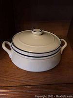 Front view of the cream-colored stoneware casserole dish with lid and blue stripe accents.