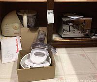 Moulinex food processor and attachments arranged with manual, Lagostina toaster next to food processor in wooden shelf cubby.