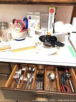 Overview photo showing cookie press box, mixing bowls, rolling pin, measuring cups, glass jars, and partially opened drawer with flatware.