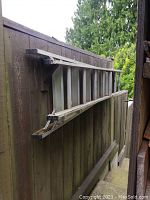 Side view of aluminum multi-position ladder hanging against a wooden fence, showing its full length and rungs.