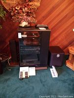 Full view of the entertainment cabinet with front glass doors showing AV components inside, including Yamaha receiver and speakers on the sides, plus subwoofer on the right.