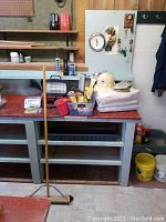 Overall view of workbench with broom, white hard hat, folded work blankets, plastic bin with tools and supplies, keys not included