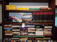 Wide view of multiple shelves filled with mixed books including Popular Mechanics encyclopedia set in black and red.