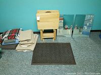Photo showing wooden TV trays with foldable legs, folded blankets, two rectangular mirrors with one corner broken, and dark brown herringbone floor mat.
