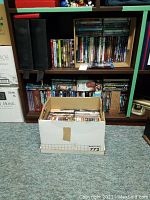 Cardboard box filled with DVDs, lower shelves holding additional cases