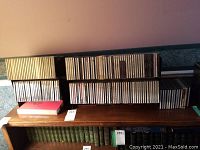 Wide shot of multiple rows of classical music CDs arranged on a wooden surface above green hardcover books.